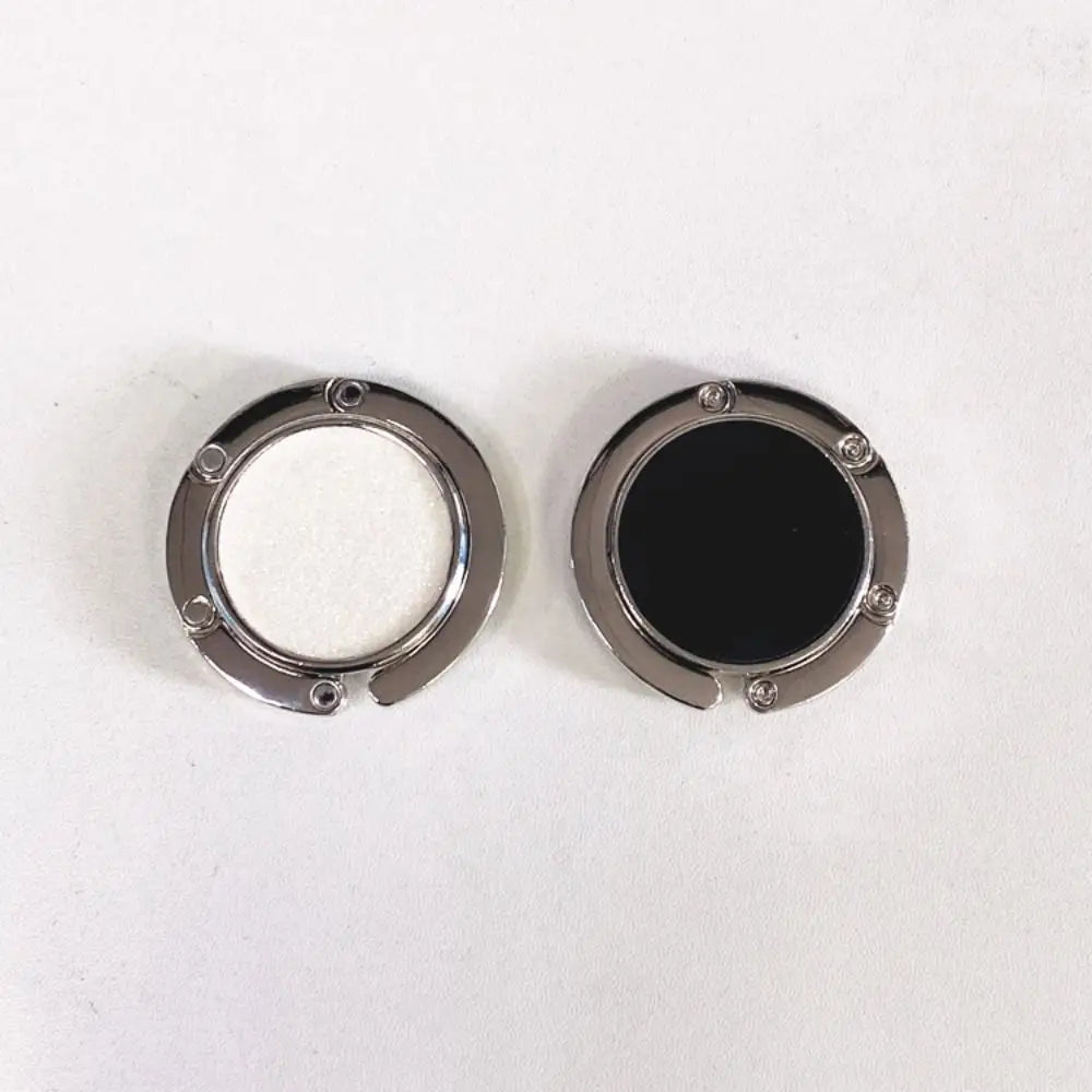 A pair of metal desk hooks with circular openings, one containing white material and the other black material.