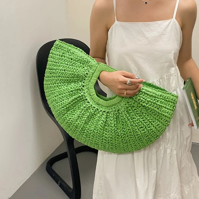 A woman holds a bright green crocheted half-moon beach handbag against a white dress.
