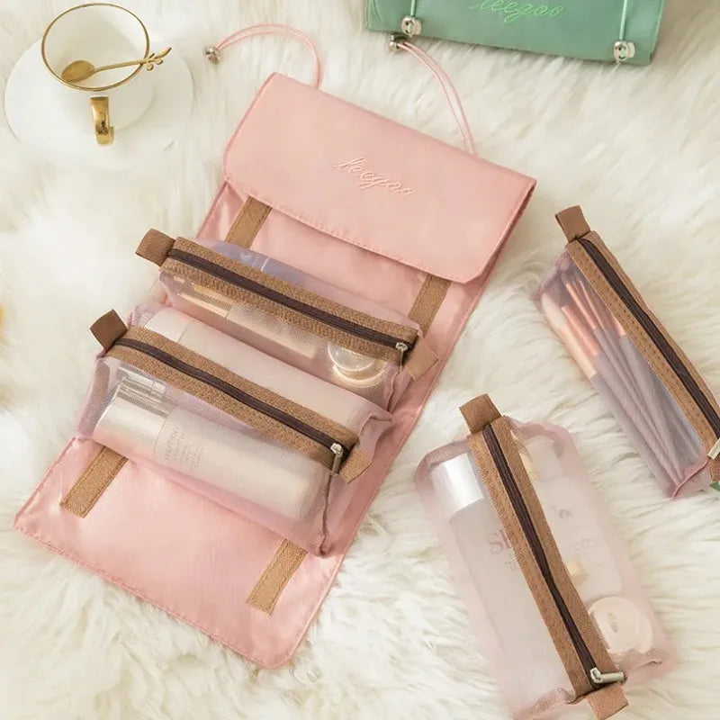 A pink portable detachable makeup bag with a beige strap and clear cosmetic pouches resting on white fluffy material.