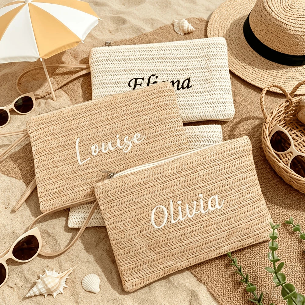 Three handwoven straw makeup bags with names Flora, Louise, and Olivia resting on sand.