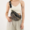 Eine Frau trägt ein cremefarbenes geripptes Crop-Top und beige Hosen und hält eine leopardprintierte Crossbody-Tasche.