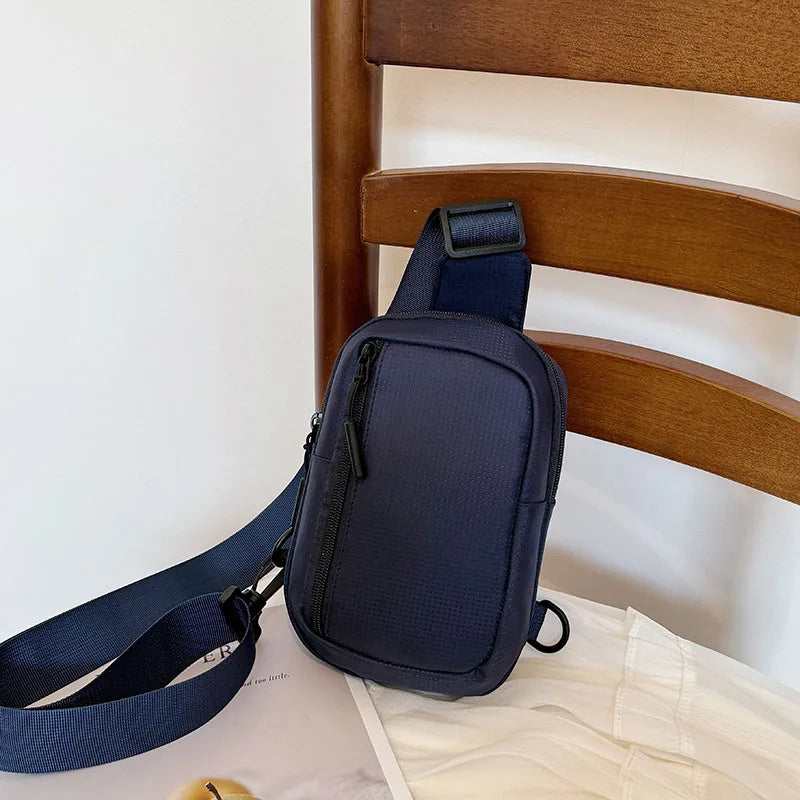 A dark blue chest bag with a strap is resting on a wooden bed frame.