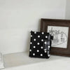 Black leather polka dot passport holder with multi-card slots displayed in front of a framed sketch.