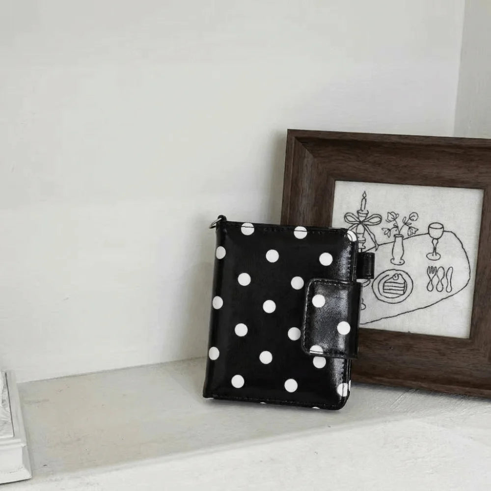 Black leather polka dot passport holder with multi-card slots displayed in front of a framed sketch.