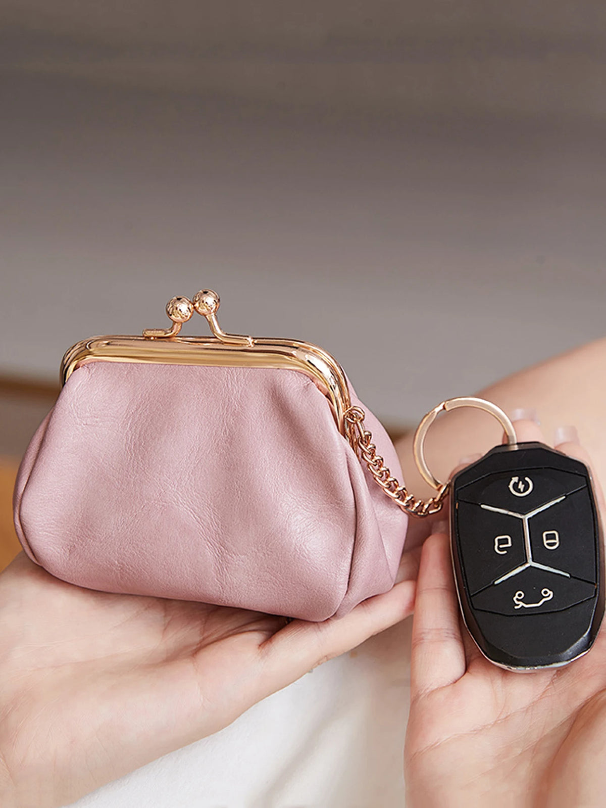 A pink leather coin purse with a gold-tone clasp and chain attached to a black keychain is held in a hand.