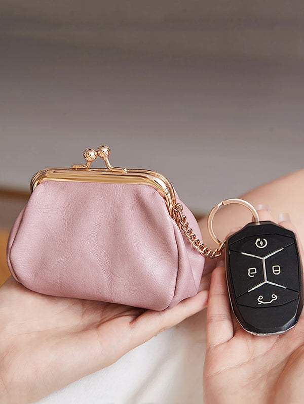 A pink leather coin purse with a gold-tone clasp and chain attached to a black keychain is held in a hand.
