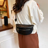 A woman wearing a cream blouse and brown skirt holds a black PU leather crossbody bag.