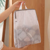 A hand is holding a white honeycomb mesh laundry bag with gray handles against a wooden background.