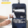 A dark blue toiletry bag is shown with a hanging hook, and a hand is holding a white cup.