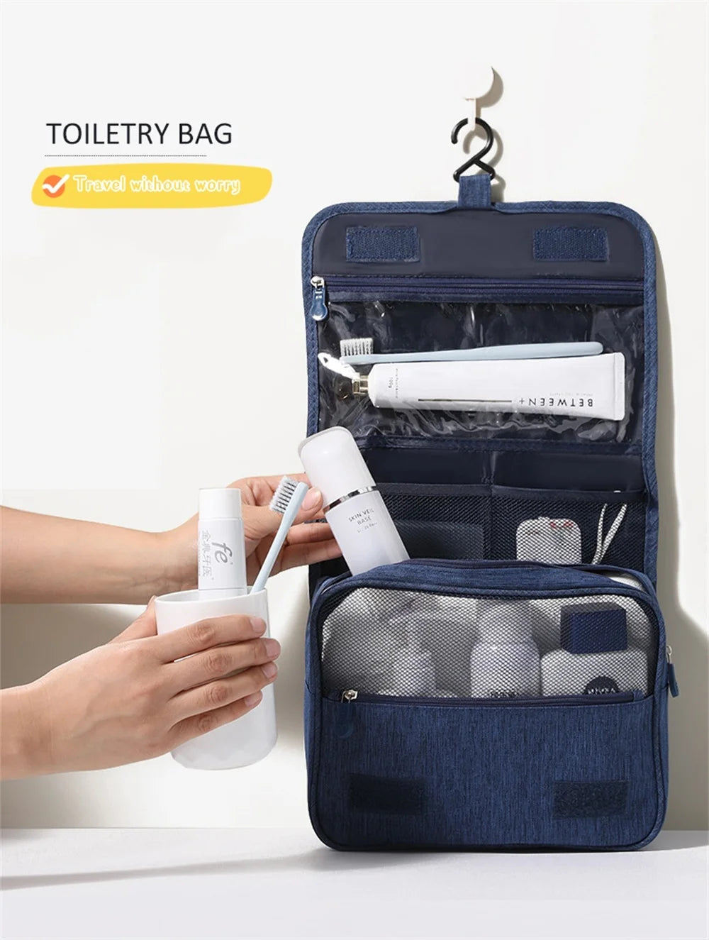 A dark blue toiletry bag is shown with a hanging hook, and a hand is holding a white cup.