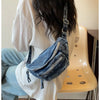 Une personne tient un sac bandoulière en denim vintage lavé contre un t-shirt blanc, à côté d'une chaise de couleur claire.