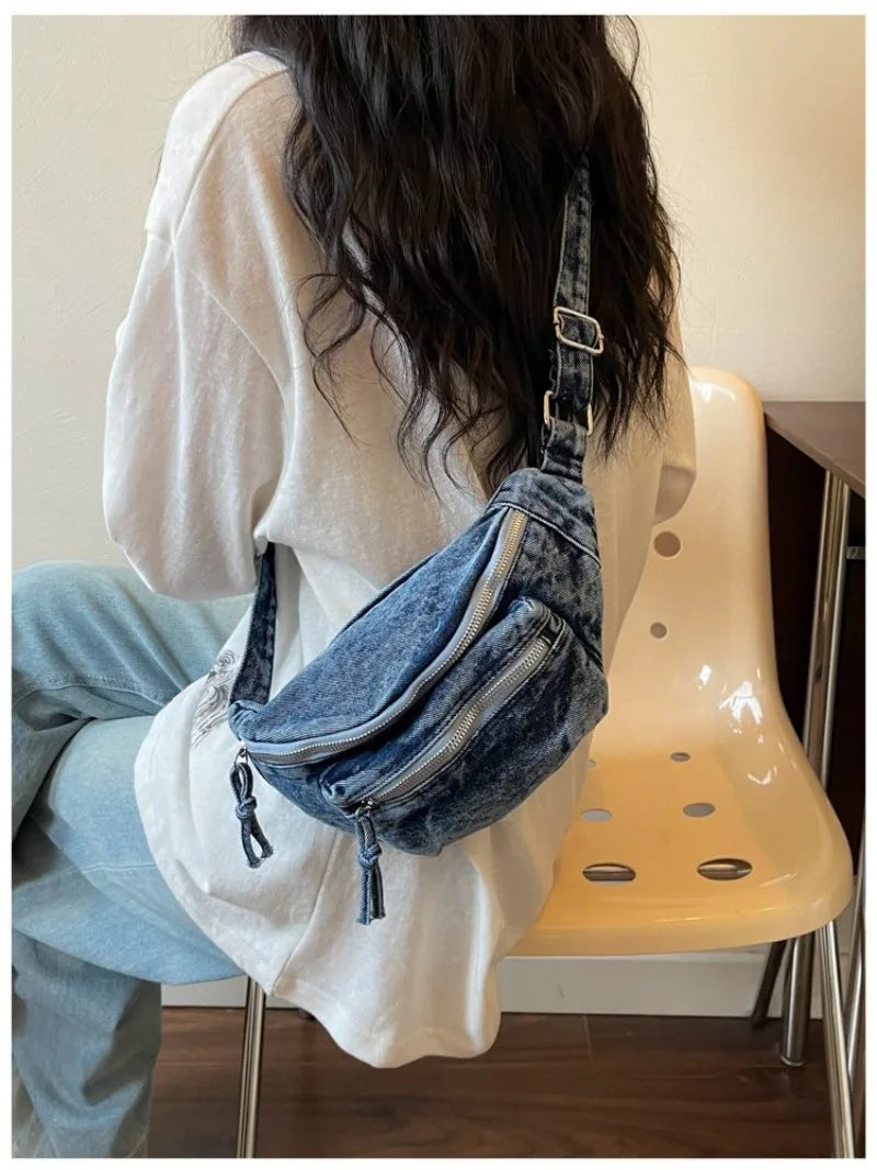 Une personne tient un sac bandoulière en denim vintage lavé contre un t-shirt blanc, à côté d'une chaise de couleur claire.