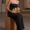 A woman wearing a black dress holds a gold acrylic chain crossbody bag.