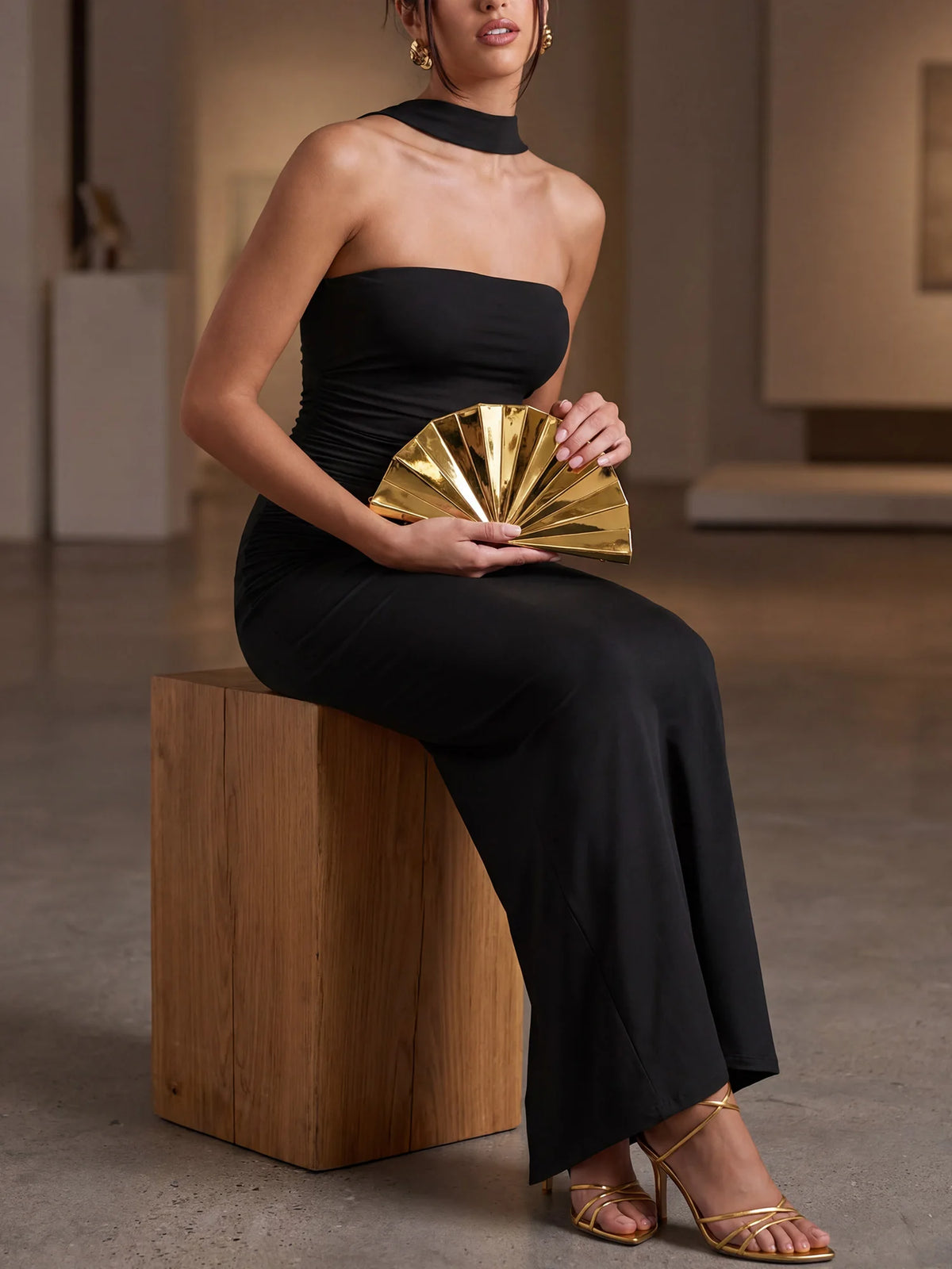 A woman wearing a black dress holds a gold acrylic chain crossbody bag.
