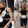 A woman models a Mini Belt Bag in beige against a dark outfit, showing its design and fit.
