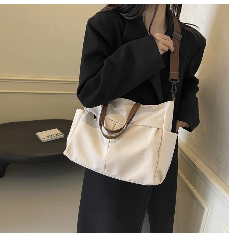 A woman holds a cream-colored lightweight nylon tote bag with brown leather straps and multiple pockets.