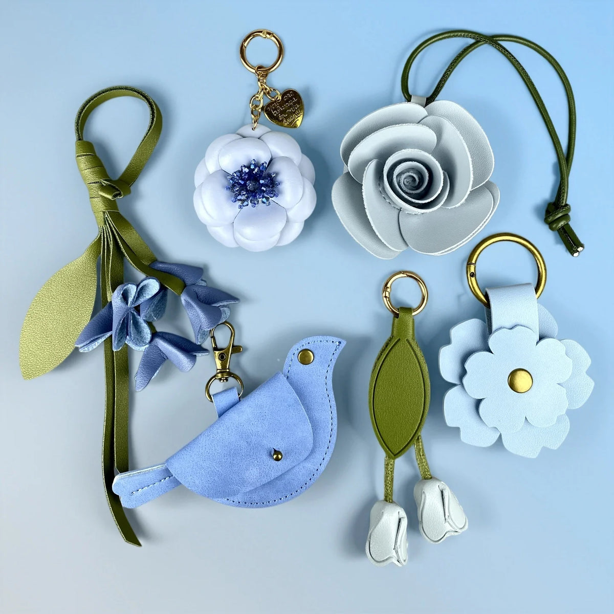A set of blue floral PU leather keychain and bag charm featuring a flower, leaves, and a small bird shape.