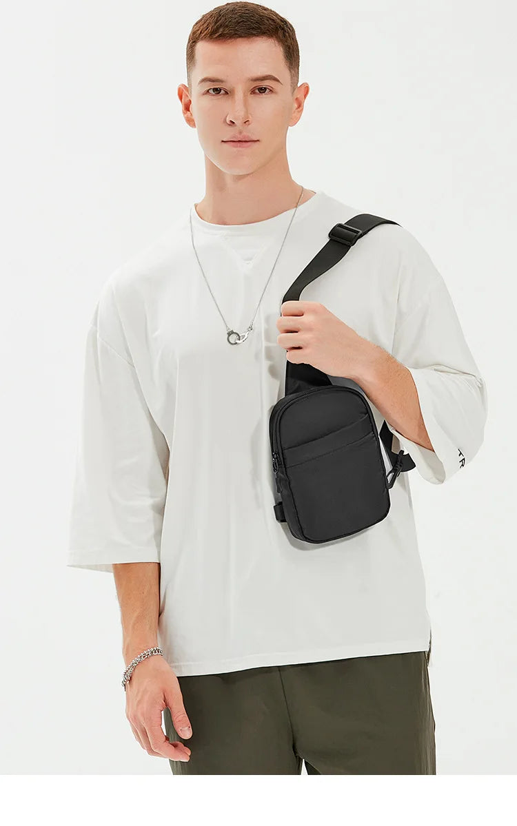 Modelo masculino vistiendo camiseta blanca y pantalones oliva, sosteniendo una bolsa cruz multifuncional negra.