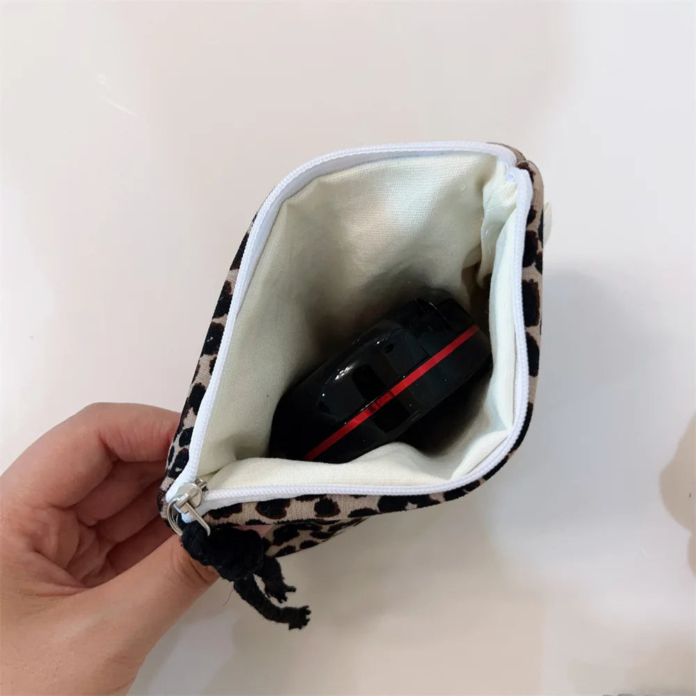 A leopard print cosmetic bag with a zipper is being held in a hand.