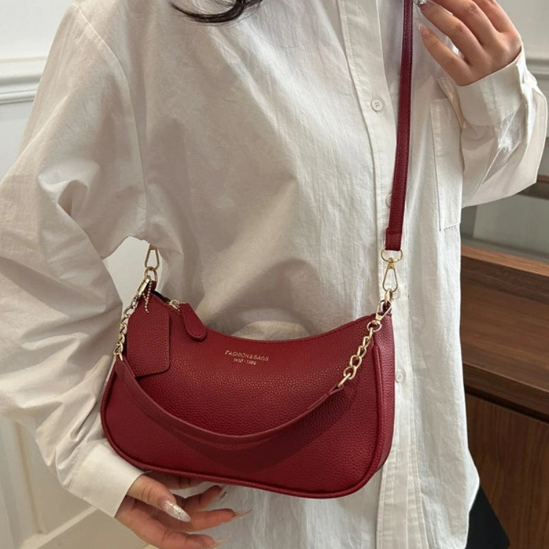 A maroon leather shoulder bag with a gold chain pendant is shown against a white shirt.