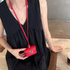 A woman holds a red leather coin purse with a gold pendant and lanyard against a black dress.