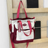 Maroon-weißes Nylon-Korbhandtasche mit rosa Trägern auf Holzregal.