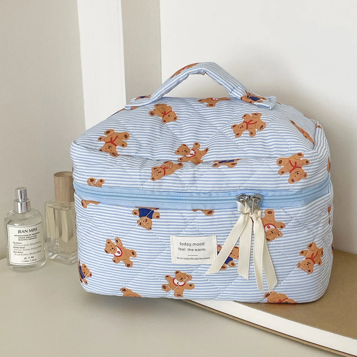 A light blue striped cosmetic makeup bag featuring bear designs and a fabric ribbon.