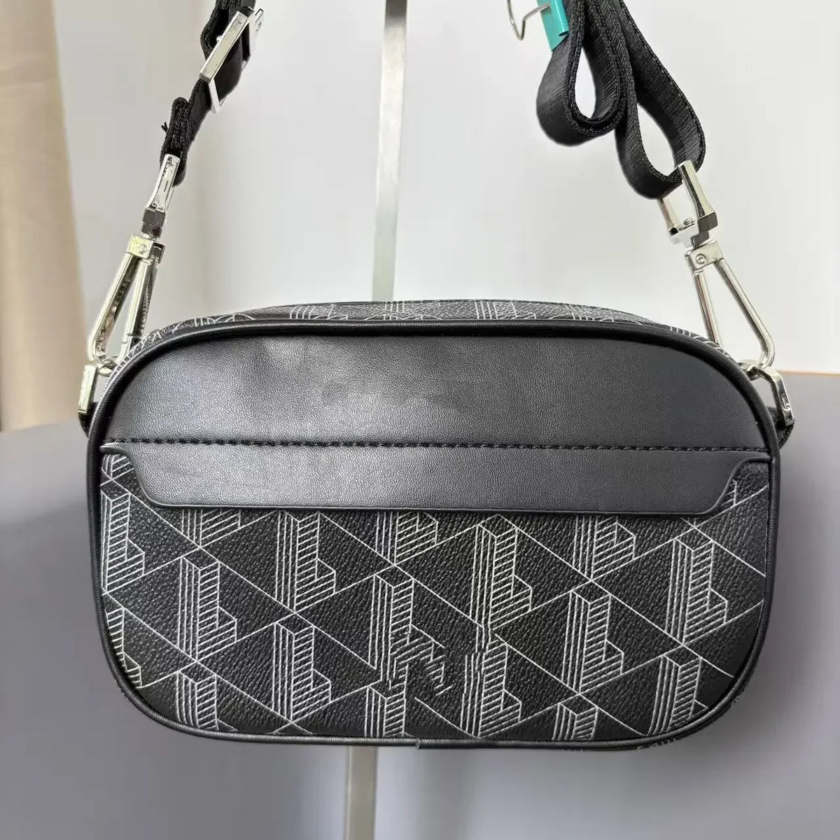 Schwarze Leder-Crossbody-Tasche für Herren mit weißem geometrischem Muster, hängt an einer silbernen Kette.
