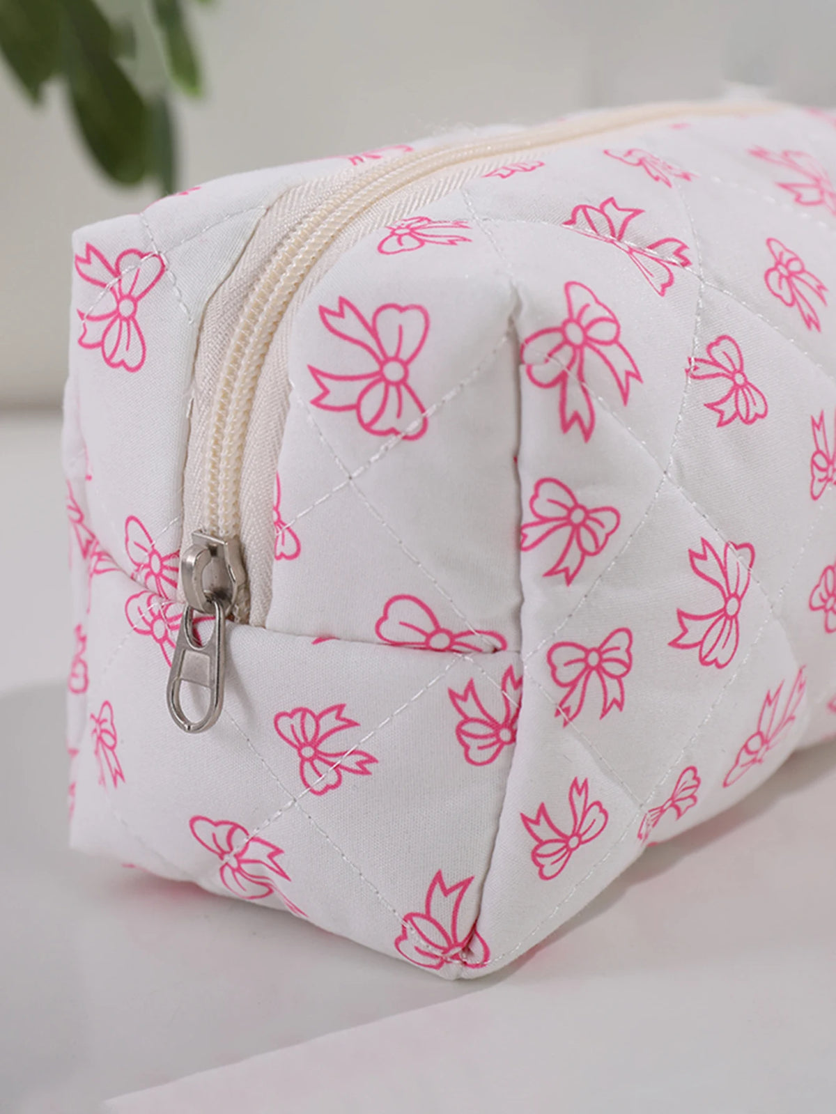 Bolsa de maquillaje blanca con estampado de lazo rosa y textura acolchada.