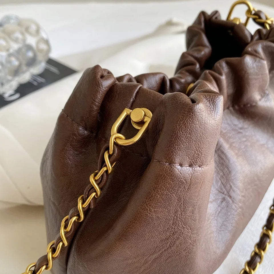 A close-up of a brown PU leather chain shoulder bag with gold hardware and a leather strap.