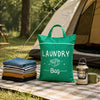 A bright green laundry bag with a box graphic rests on a picnic blanket outdoors next to a tent and a lantern.
