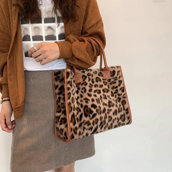A woman holds a brown leopard print faux fur designer shoulder tote bag against a white background.