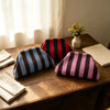 A close-up of an elegant knit cloud makeup bag with vertical stripes in black, red, and purple resting on a wooden table.