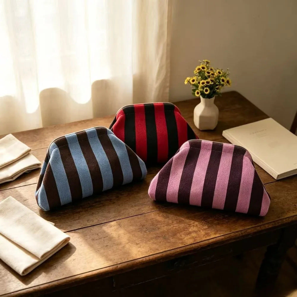 A close-up of an elegant knit cloud makeup bag with vertical stripes in black, red, and purple resting on a wooden table.