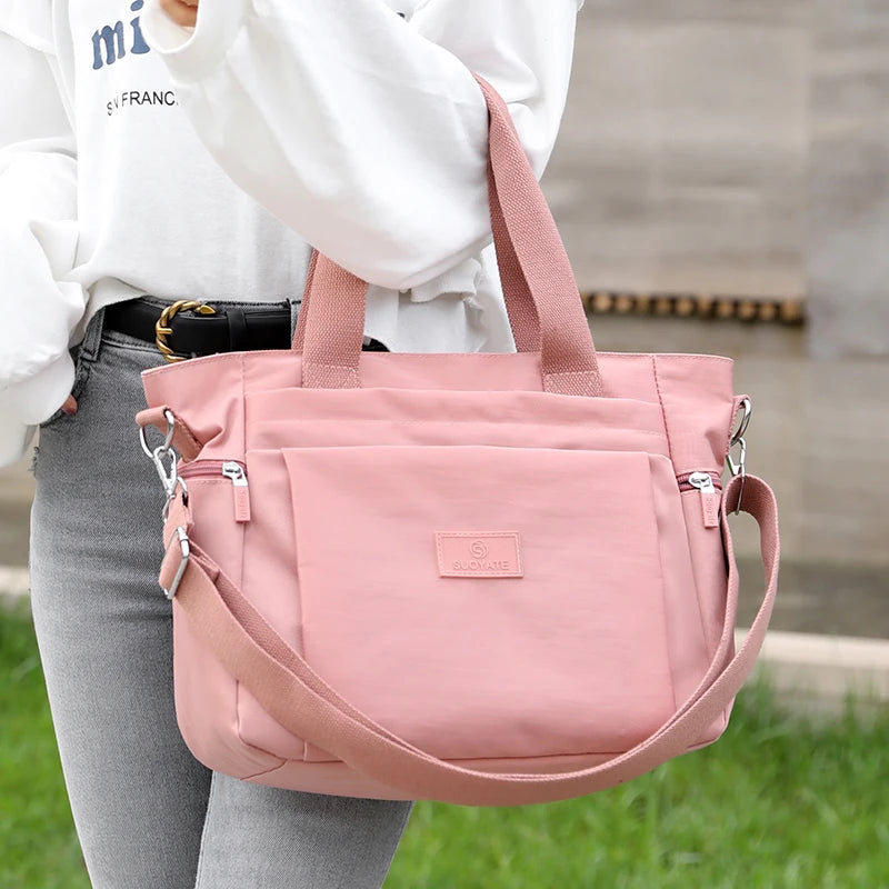 A person holds a pink durable nylon tote bag with a secure zipper closure against a blurred outdoor background.