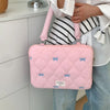 Bolso de portátil acolchado rosa con detalles de lazo azul, sostenido por una persona con camisa blanca y jeans.