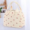 A beige corduroy lunch bag with a fabric handle and small red strawberry pattern.