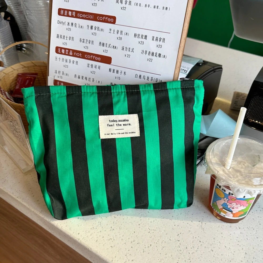 Una bolsa de almacenamiento de lona a rayas negras y verdes se muestra en una encimera junto a una taza.