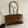 A brown leather tote bag with a handle is displayed on a white textured surface next to folded cream-colored paper.