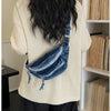 Une personne portant un pull tricoté crème et un pantalon foncé tient un sac bandoulière en denim délavé vintage.