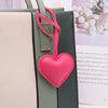 A pink leather heart charm attached to a green and white striped bag, used as a keychain.