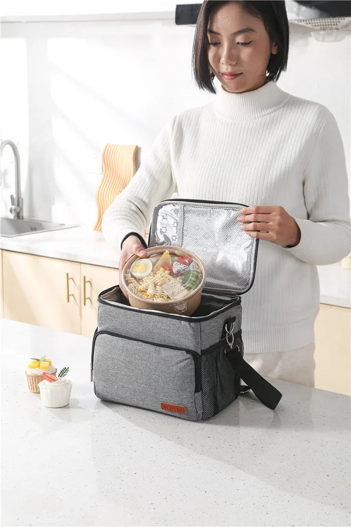 A woman holds an insulated thermal lunch bag containing food on a kitchen counter.