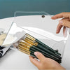 A hand holds a transparent organizer pouch with several gold and black cosmetic brushes inside.