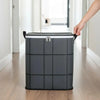 A hand is lifting a gray fabric storage organizer bag with a black handle in a bright hallway.