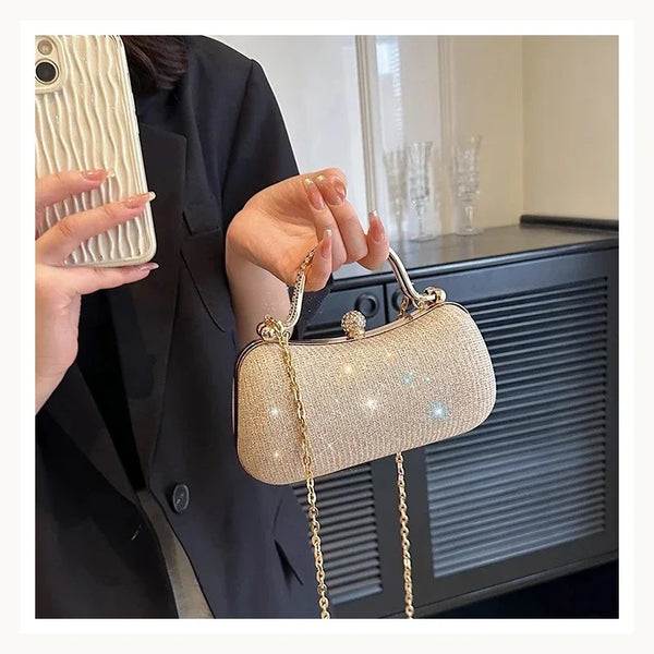 A hand holds a gold glitter crossbody evening clutch bag against a dark background.