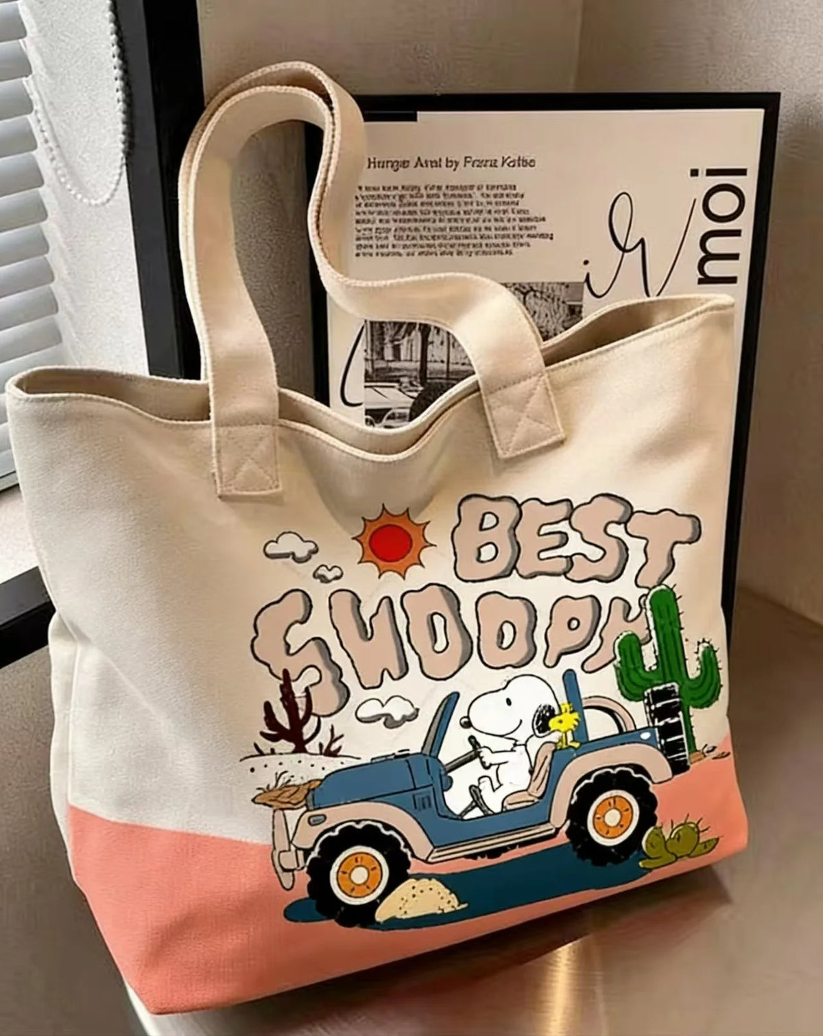 A beige canvas shoulder bag featuring a Snoopy cartoon design of a blue jeep and a cactus.