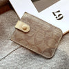 A gold-toned PU leather card holder purse resting on a gray knitted fabric next to a white card.