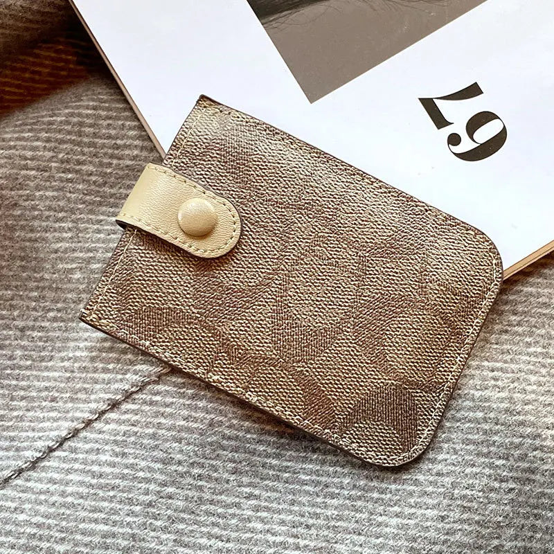 A gold-toned PU leather card holder purse resting on a gray knitted fabric next to a white card.