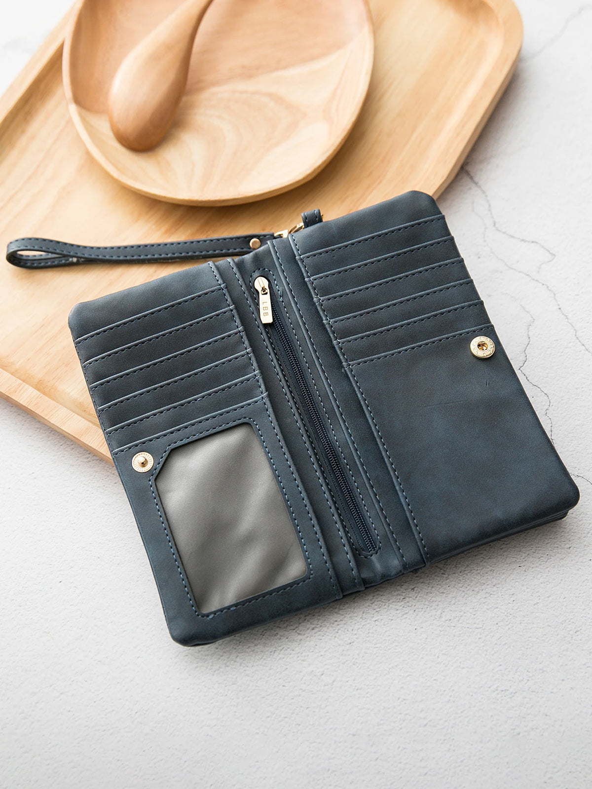 A dark gray leather wallet with a double zipper and card slots rests on a light wooden board.
