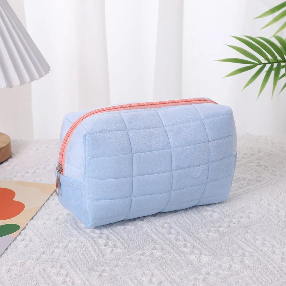 Light blue quilted velvet cosmetic and toiletry bag resting on a white textured surface.